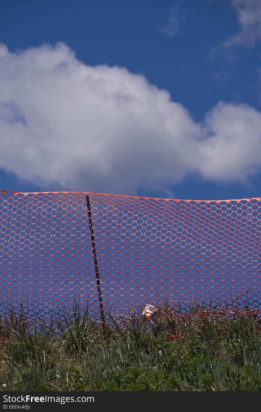 Orange construction fence on grassy hill with blue sky and puffy white clouds. Orange construction fence on grassy hill with blue sky and puffy white clouds