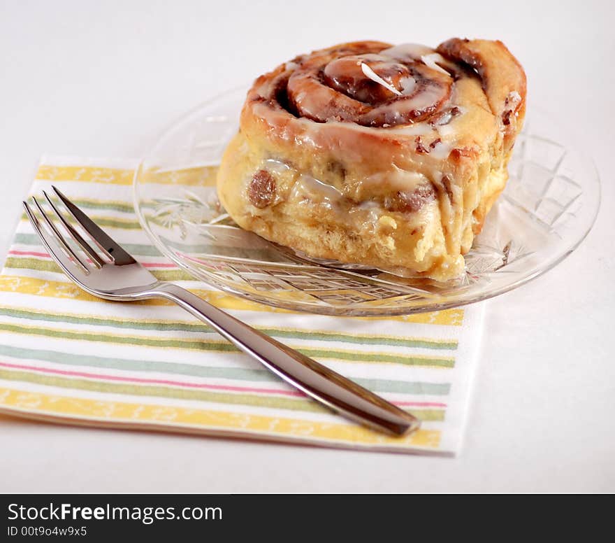 A cinnamon bun, displayed on a glass plate, striped napkin