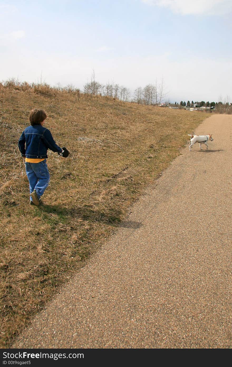 A young boy taking his dog for a walk in an urban park. A young boy taking his dog for a walk in an urban park