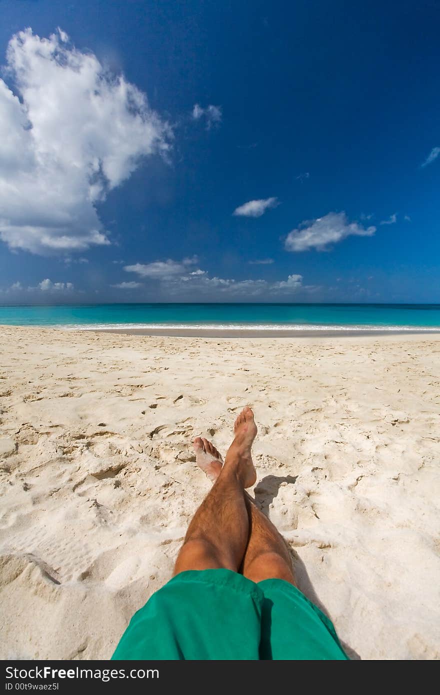 Lone man sitting on white sand beach by turquoise waters on tropical island. Lone man sitting on white sand beach by turquoise waters on tropical island