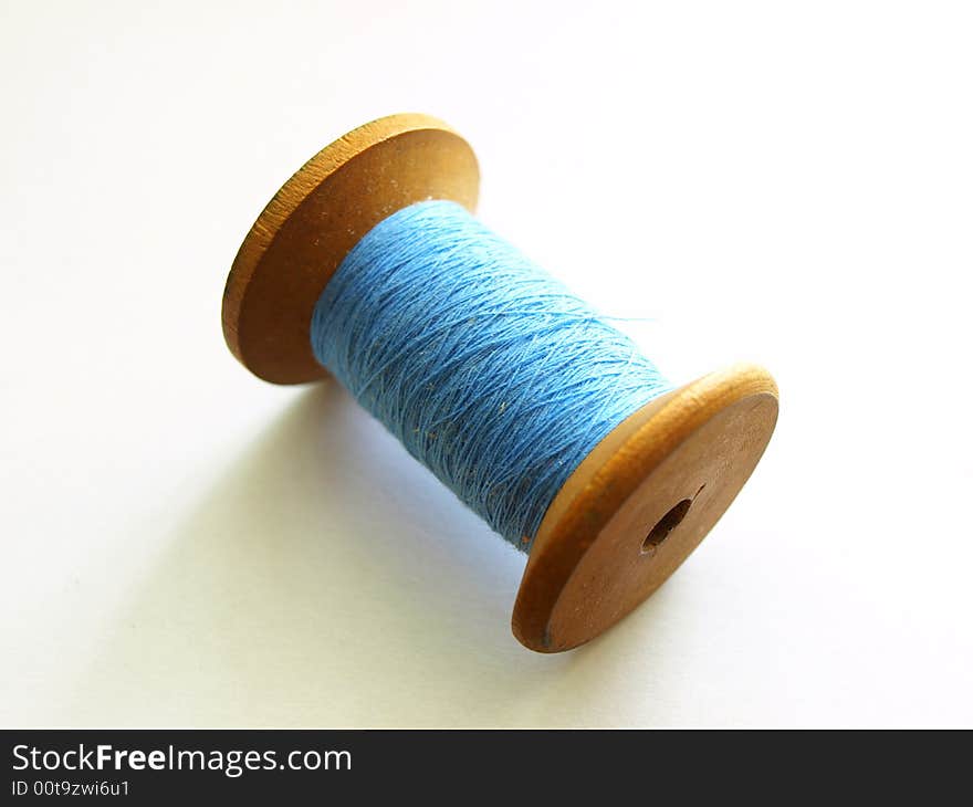 Photo of wooden bobbin with blue, cotton thread. Photo of wooden bobbin with blue, cotton thread