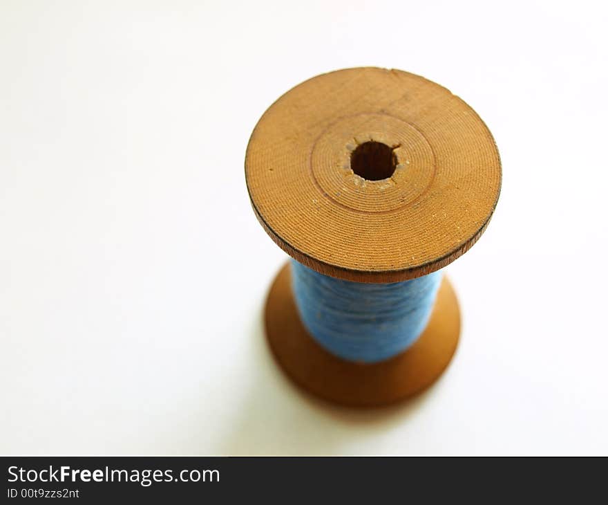 Photo of wooden bobbin with blue, cotton thread. Photo of wooden bobbin with blue, cotton thread