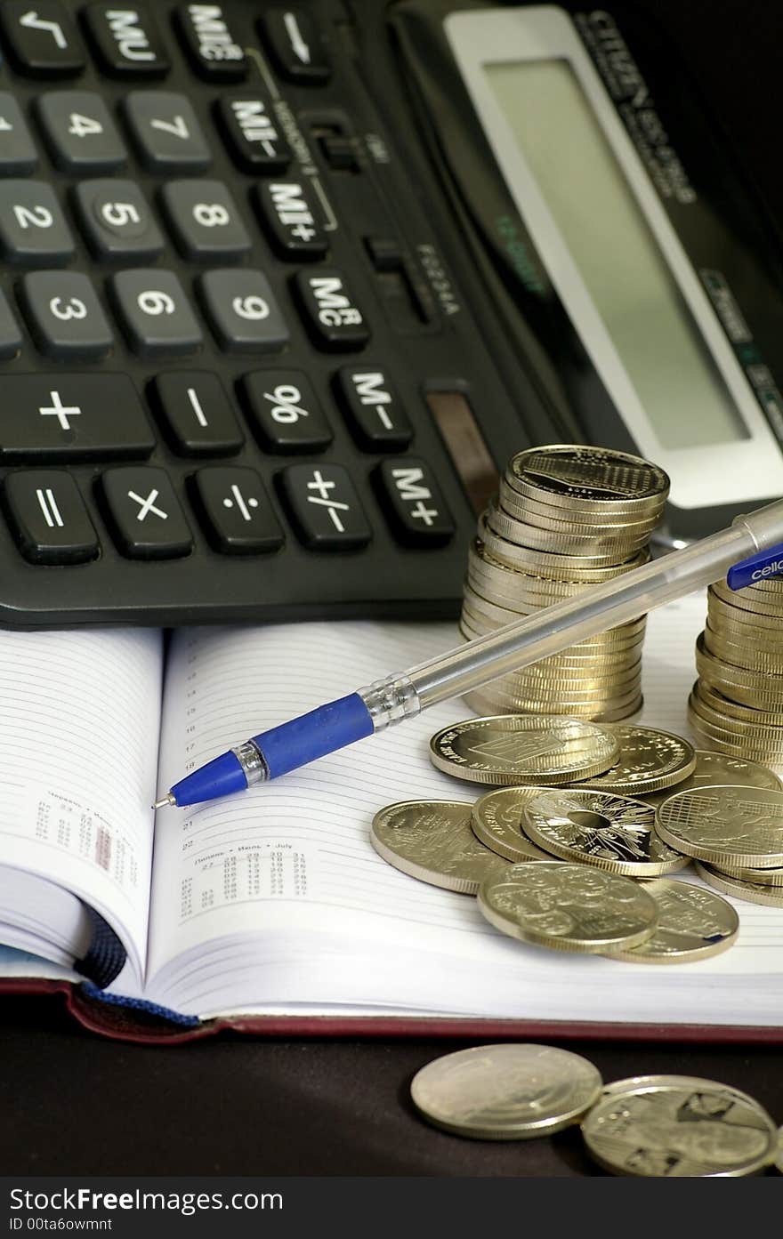 On the black background lies the notebook and many silver coins, and so there is a calculator. On the black background lies the notebook and many silver coins, and so there is a calculator.