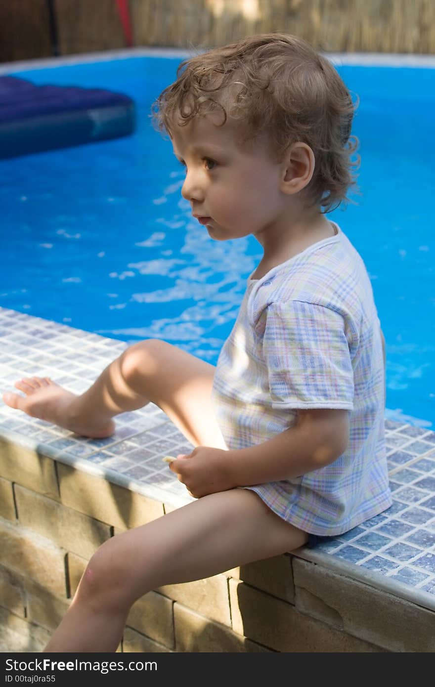 A curly white boy sits in a reverie on skirting of pool. A curly white boy sits in a reverie on skirting of pool