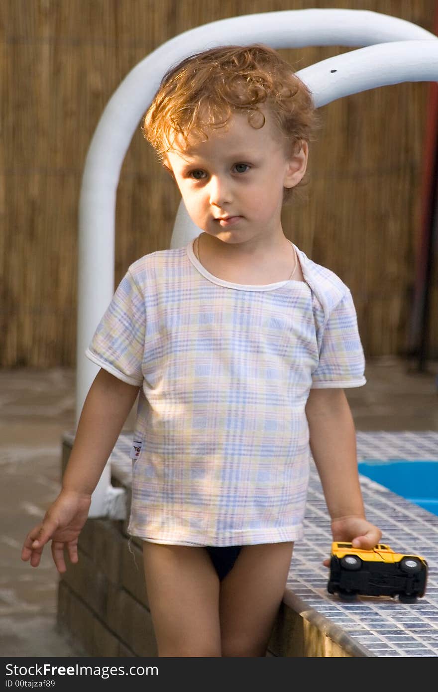 A curly little boy plays with the toy car of white and yellow color at a pool. A curly little boy plays with the toy car of white and yellow color at a pool