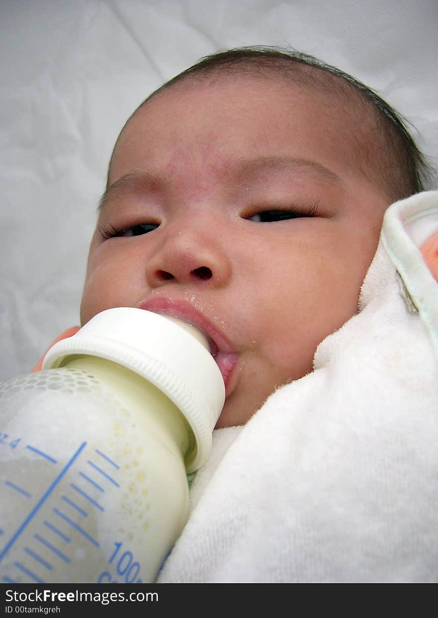 Asian baby holding milk feeding bottle with head leaning isolated bare headed. Asian baby holding milk feeding bottle with head leaning isolated bare headed