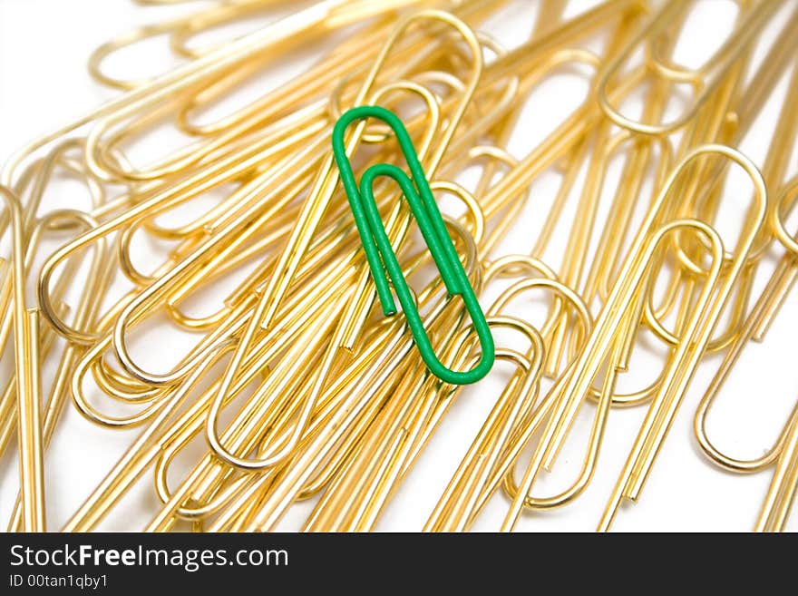 Golden paper clips and one green on the white isolated background