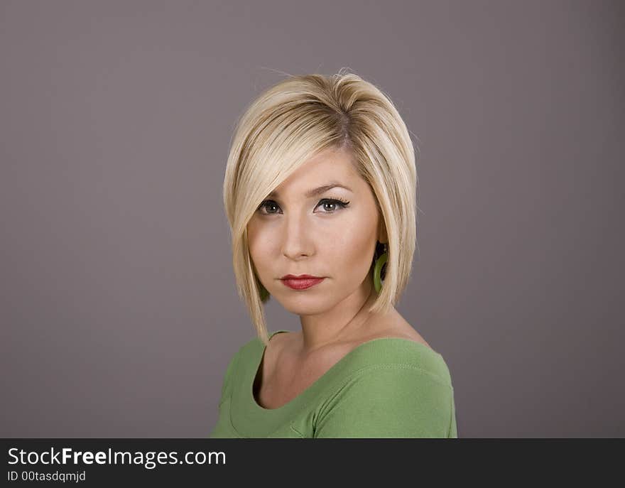 A pretty blonde girl in a green blouse with sad eyes against a grey background. A pretty blonde girl in a green blouse with sad eyes against a grey background