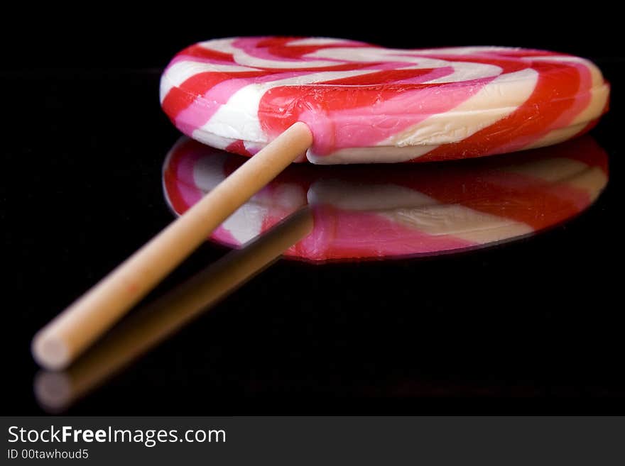 Heart lollipop on black background with reflection.