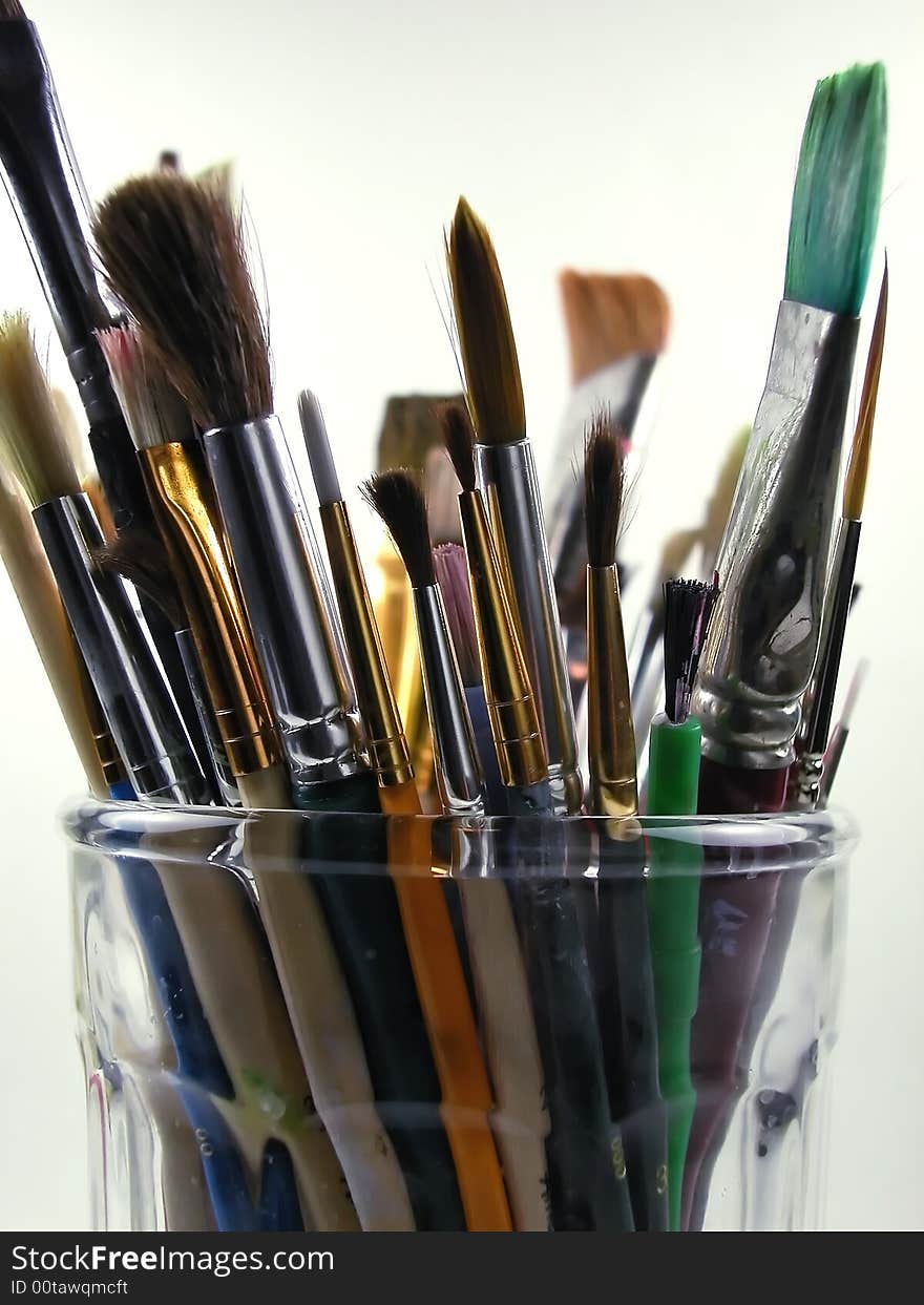 Close-up shot of a glass full of messy, used paint brushes against a light background. Close-up shot of a glass full of messy, used paint brushes against a light background