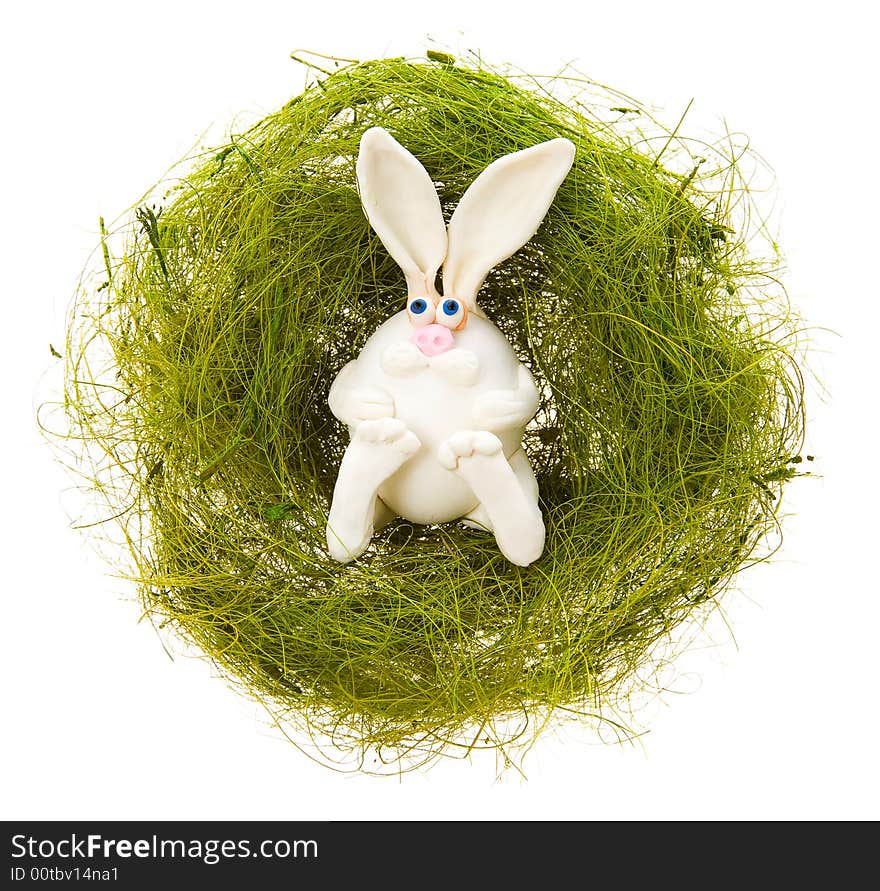 Easter toy white rabbit in a nest from a green grass on a white background. Easter toy white rabbit in a nest from a green grass on a white background