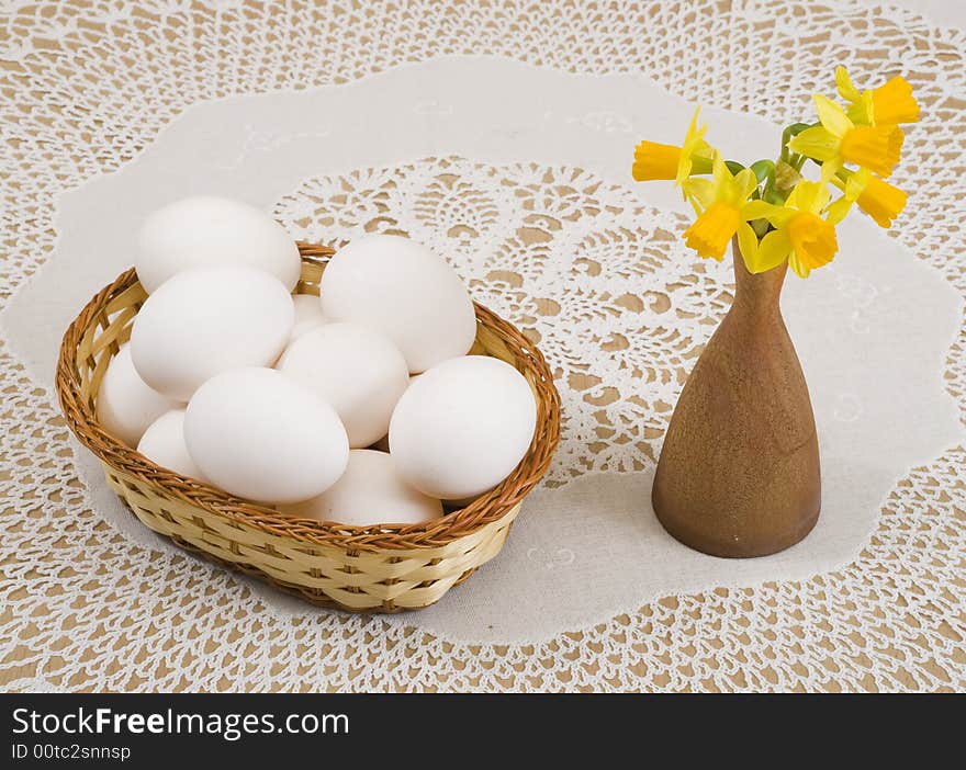 A basket of eggs and yellow daffodils in a vase. A basket of eggs and yellow daffodils in a vase