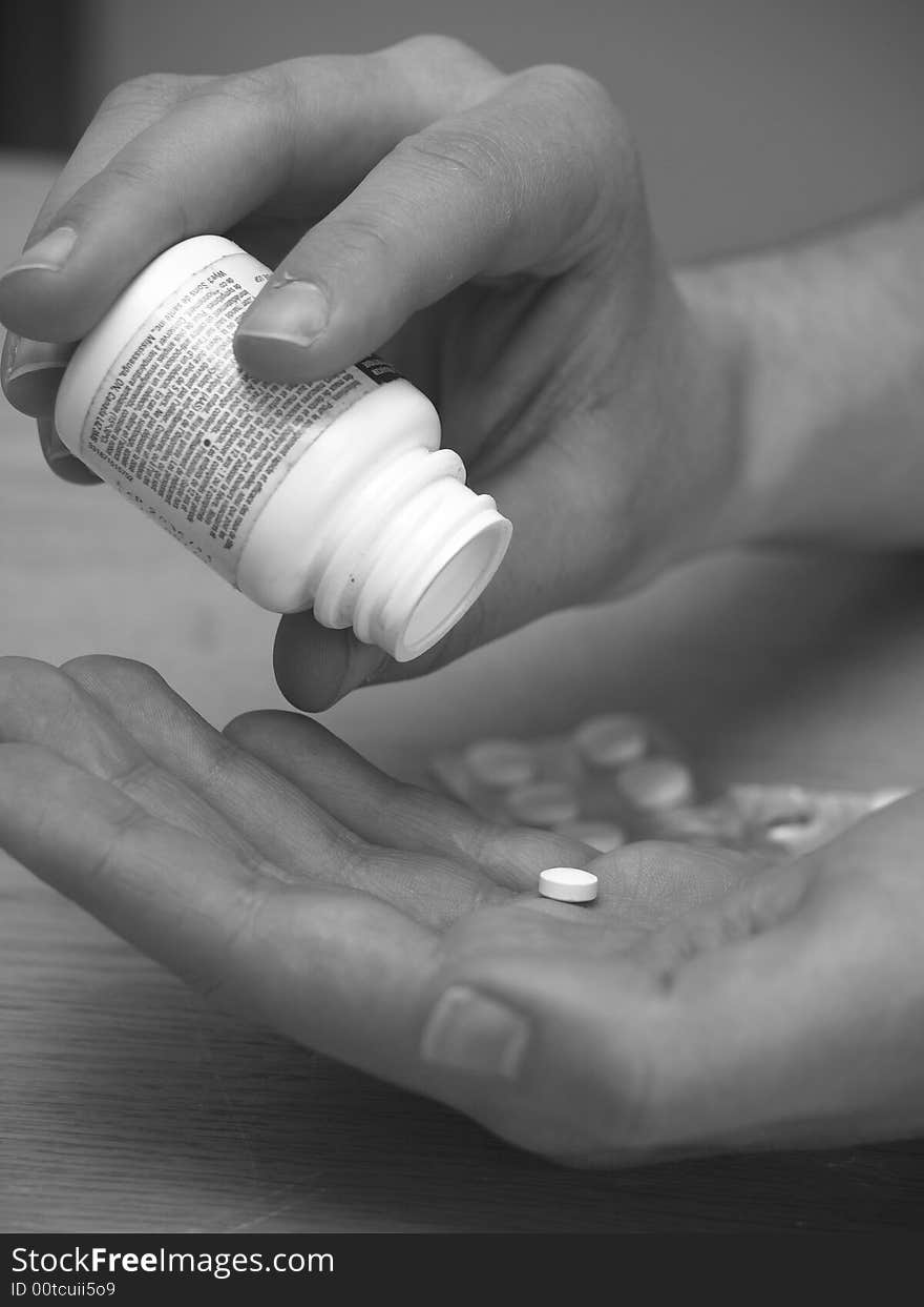 A hand holding a jar and shaking out a pill from it. A hand holding a jar and shaking out a pill from it.