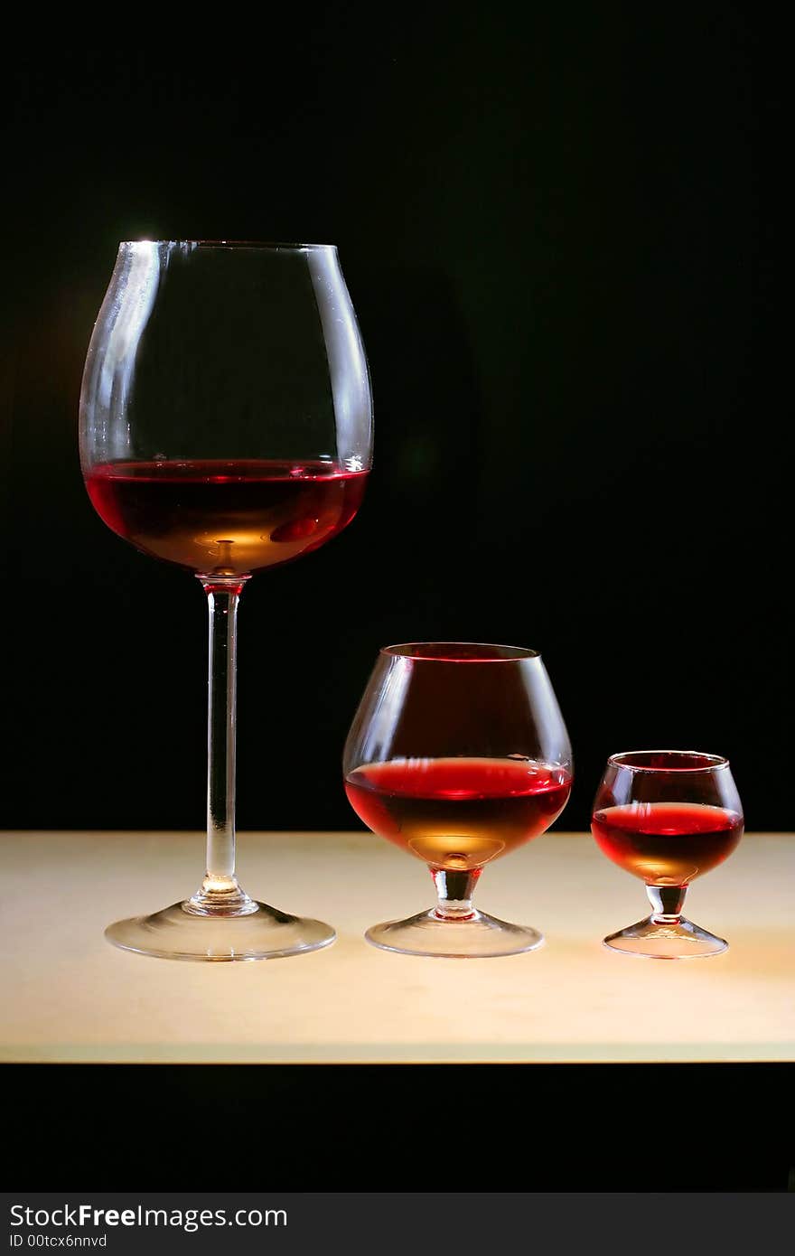 Three glasses of red wine or cognac on lighting bar and on black background.
