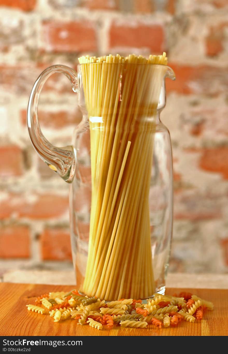 Macaroni in glass jug on brick wall background. Macaroni in glass jug on brick wall background