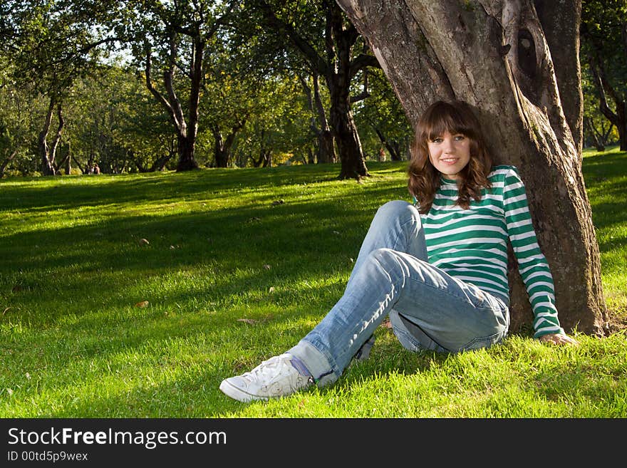 Young beautiful woman sitting at grass near tree and smiling. Young beautiful woman sitting at grass near tree and smiling