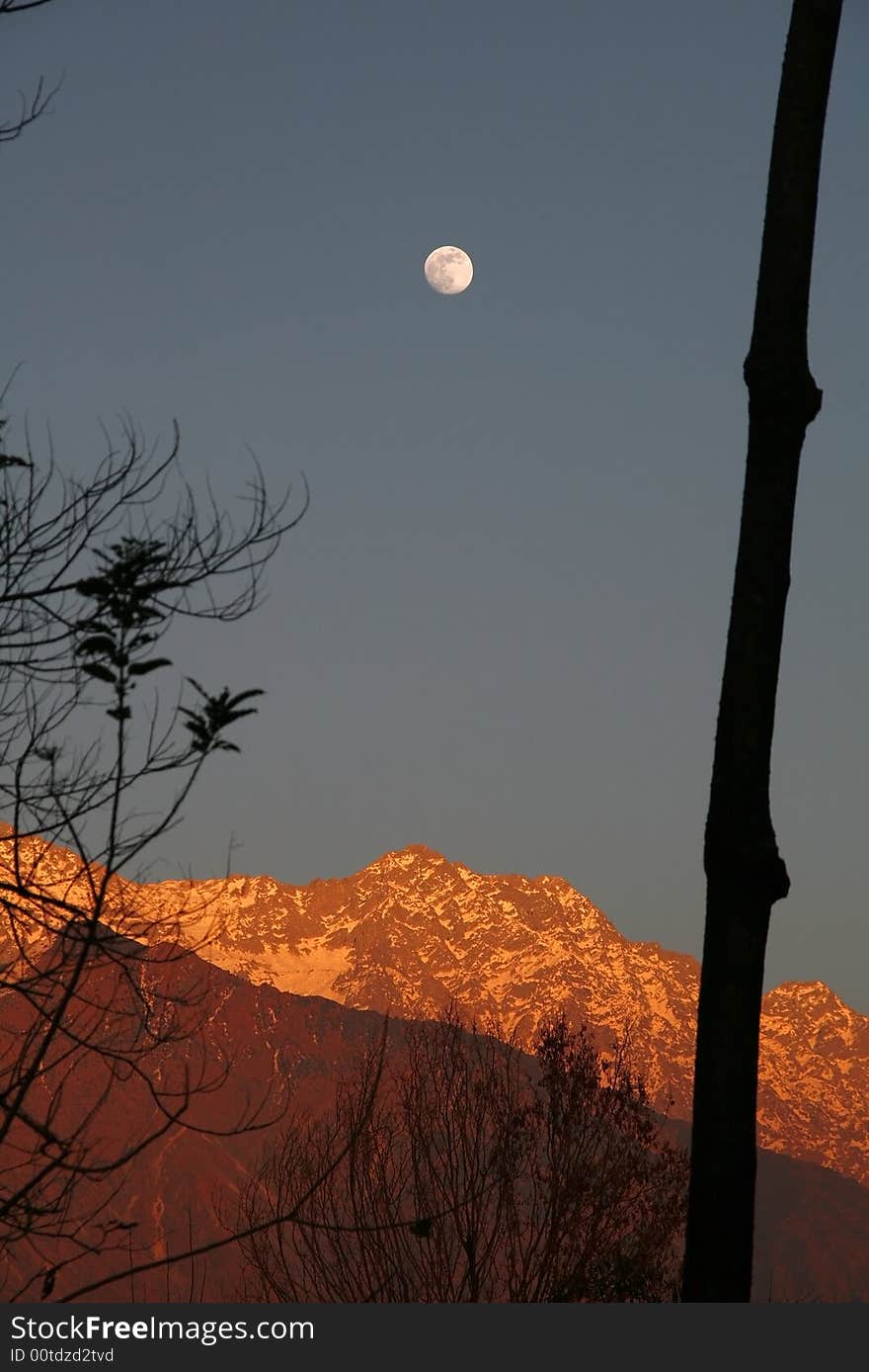 Rare image of fullmoon rise over vivid orange sunset on dhauladhar himalayan  snow peaks and mountains  as  viewed from kangra valley india. Rare image of fullmoon rise over vivid orange sunset on dhauladhar himalayan  snow peaks and mountains  as  viewed from kangra valley india