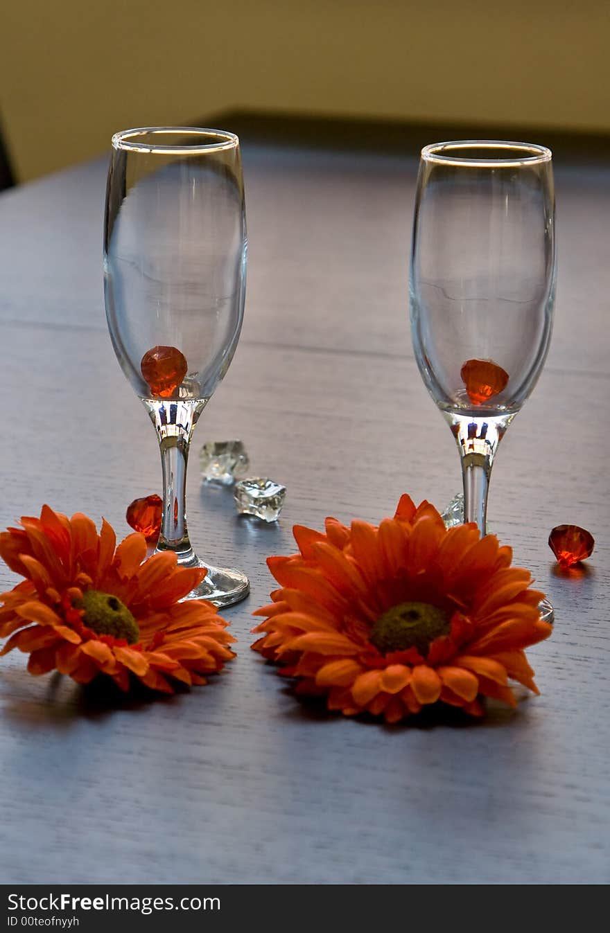 Two Wine-glass on a table near to a flowers.