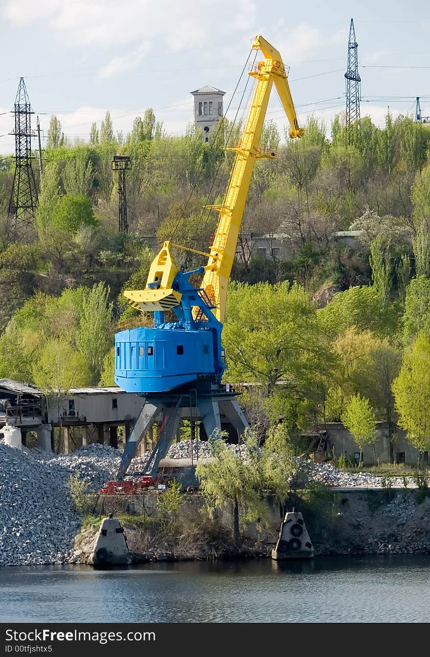 Yellow port crane on a river bank ready to load rocks. Yellow port crane on a river bank ready to load rocks