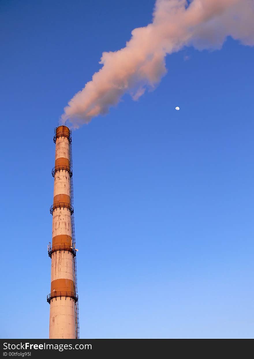 Factory pipe smoking with a white smoke and a moon nearby over the blue sky. Factory pipe smoking with a white smoke and a moon nearby over the blue sky