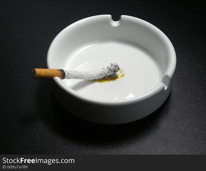 The burned down cigarette in a white ashtray on a black background