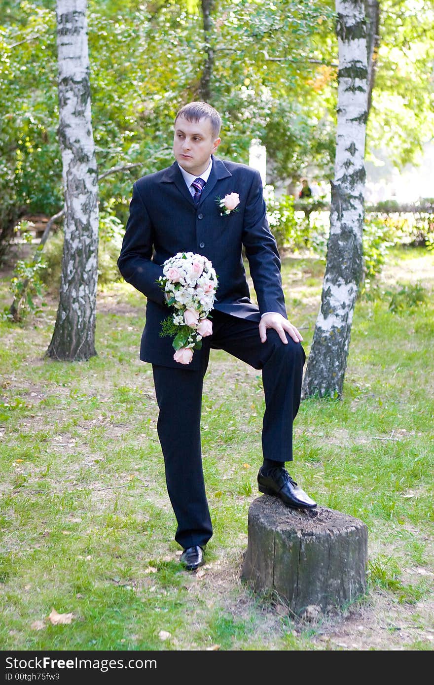 Groom with a flower bouquet waits for his bride in the park. Groom with a flower bouquet waits for his bride in the park