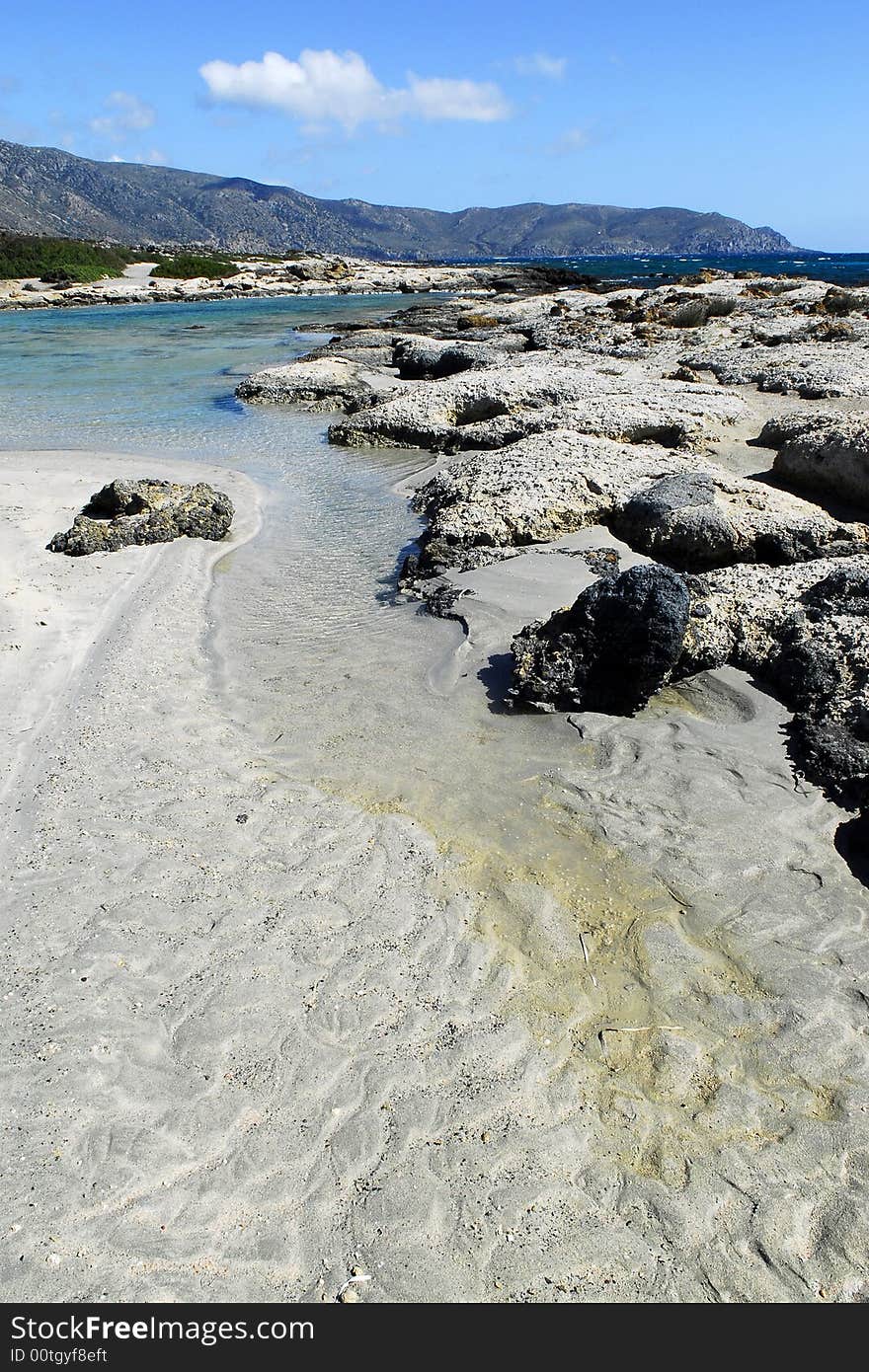 Water marks on the ssand and rocks on the shore with mountains as background. Water marks on the ssand and rocks on the shore with mountains as background