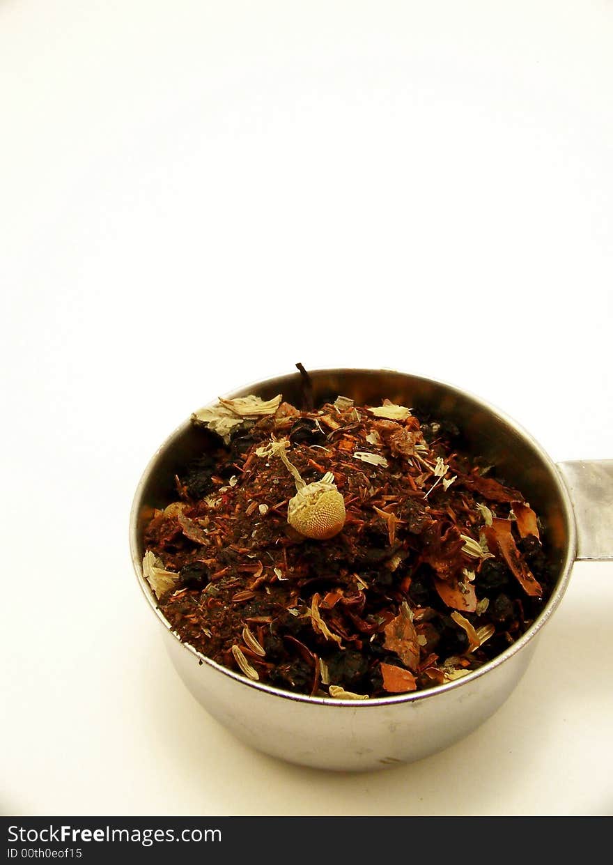 Image of mixed herbal tea in a metal measuring cup. Dried chamomile flower bud is visible on top of tea. White background. Vertical orientation. Image of mixed herbal tea in a metal measuring cup. Dried chamomile flower bud is visible on top of tea. White background. Vertical orientation.