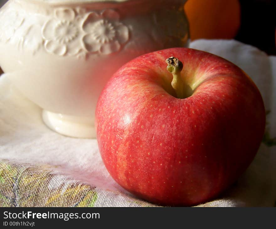 Image of a bright red apple with a plain white creamer on a tea towel in natural light.  Horizontal orientation. Image of a bright red apple with a plain white creamer on a tea towel in natural light.  Horizontal orientation.