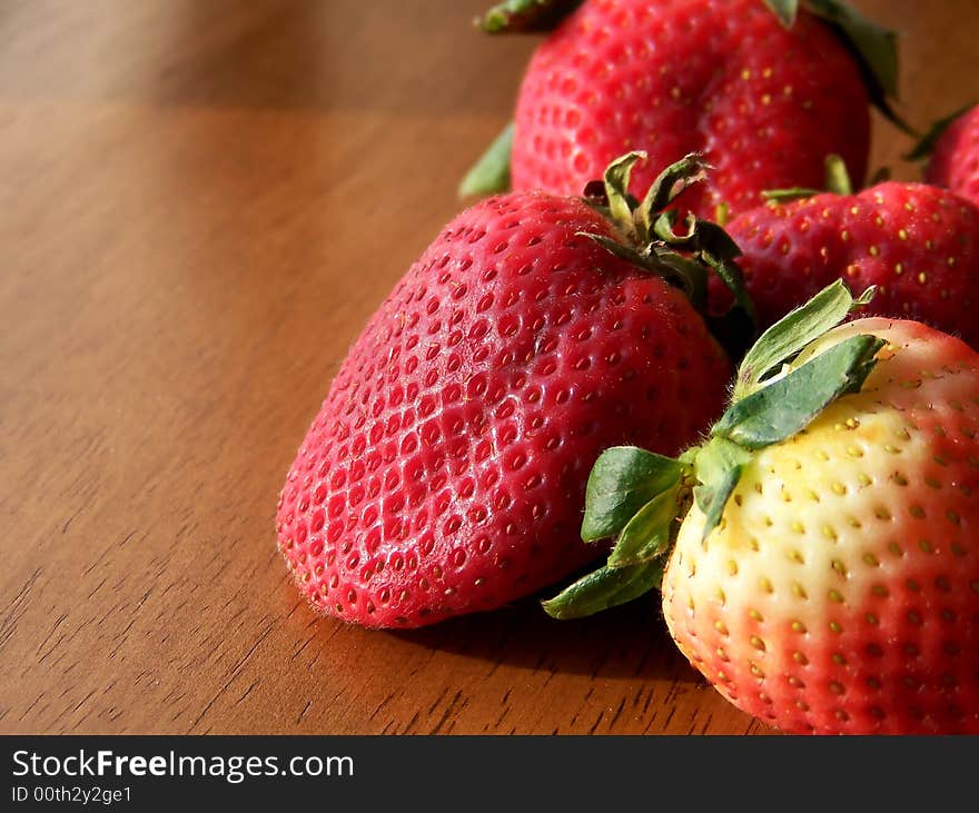 Image of red strawberries on darker wood, in natural light.  Horizontal orientation. Image of red strawberries on darker wood, in natural light.  Horizontal orientation.