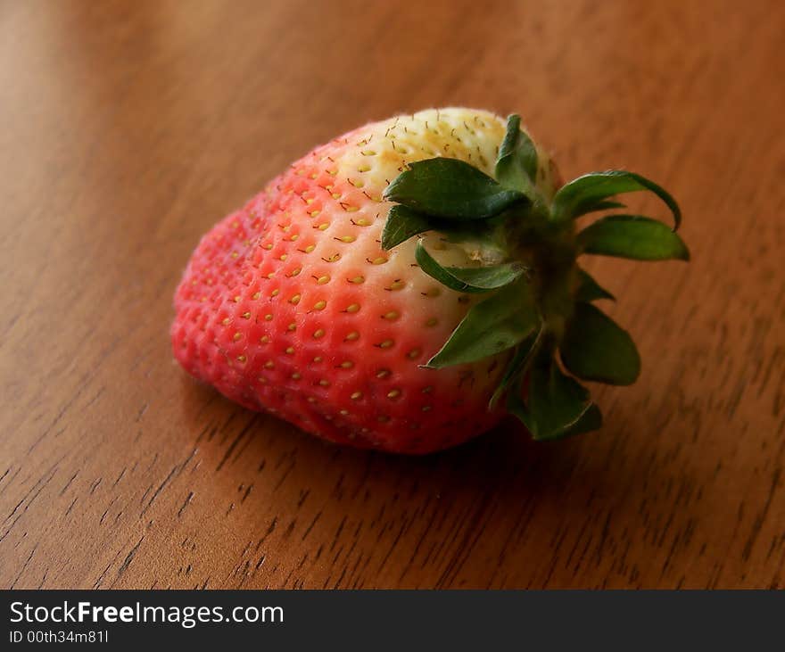 Image of a single red and white strawberry on a wooden surface, in natural sunlight.  Horizontal orientation. Image of a single red and white strawberry on a wooden surface, in natural sunlight.  Horizontal orientation.