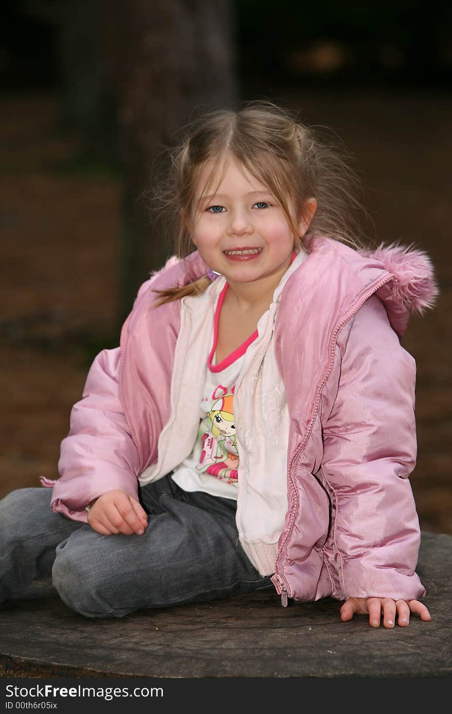 A young girl sat on a tree stump smiling at the camera. A young girl sat on a tree stump smiling at the camera