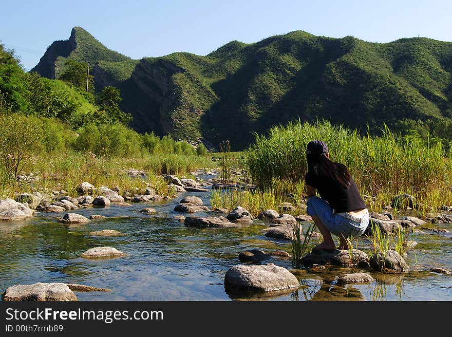 A limpid river running through the mountains,there is a beauty sitting by the water. A limpid river running through the mountains,there is a beauty sitting by the water