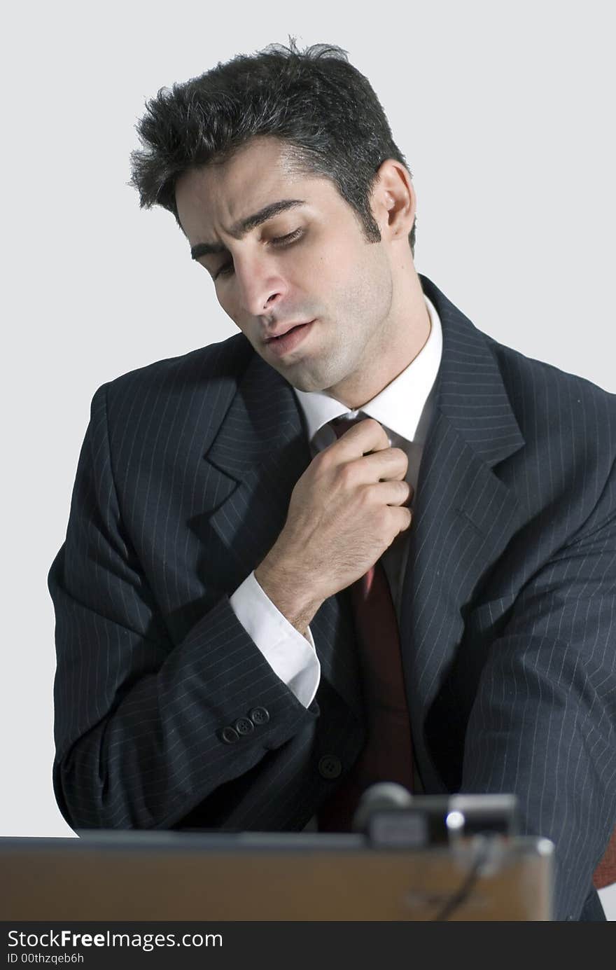 Man in a business suit loosening his tie while sitting at his laptop. Man in a business suit loosening his tie while sitting at his laptop