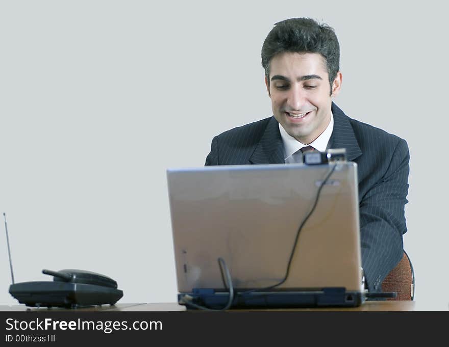 Business man working at his laptop and smiling. Isolated against a grey background. Business man working at his laptop and smiling. Isolated against a grey background