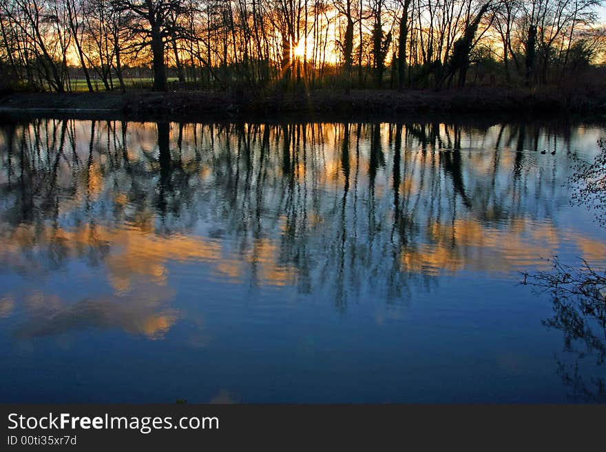 Sunset coming through the trees, reflected on the lake. Sunset coming through the trees, reflected on the lake