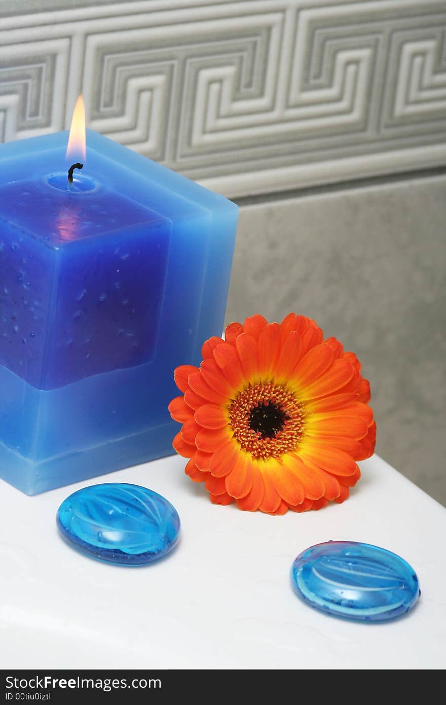 Blue candle with decorative stones and orange flower. Blue candle with decorative stones and orange flower.