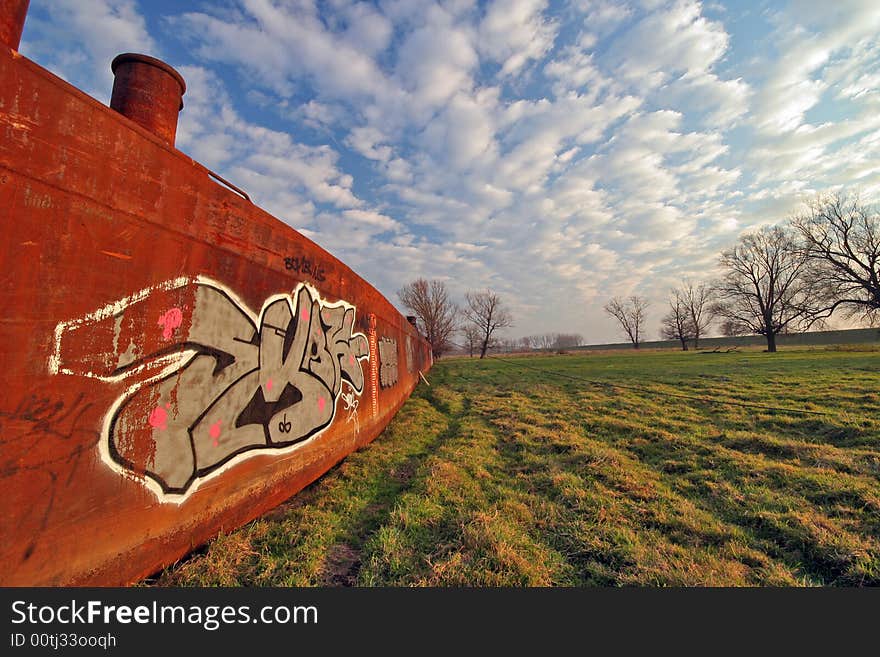 Old rusty boat on meadow with cloudy sky