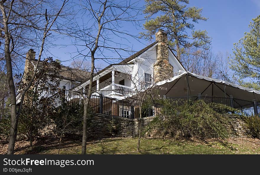 An old white board farmhouse on a hill against trees and a blue sky. An old white board farmhouse on a hill against trees and a blue sky