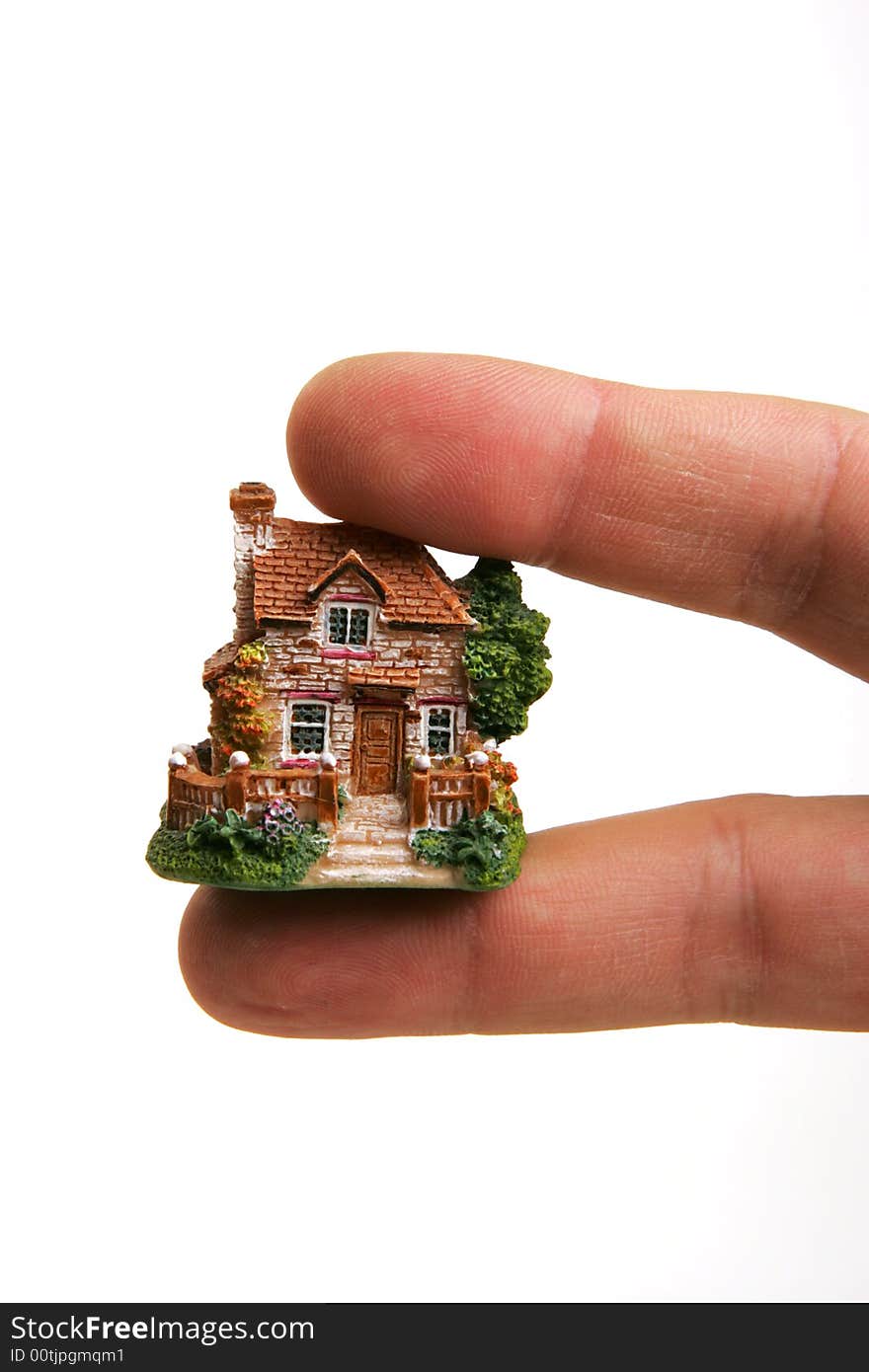 A small porcelain figurine of a country house between human fingers. A small porcelain figurine of a country house between human fingers.