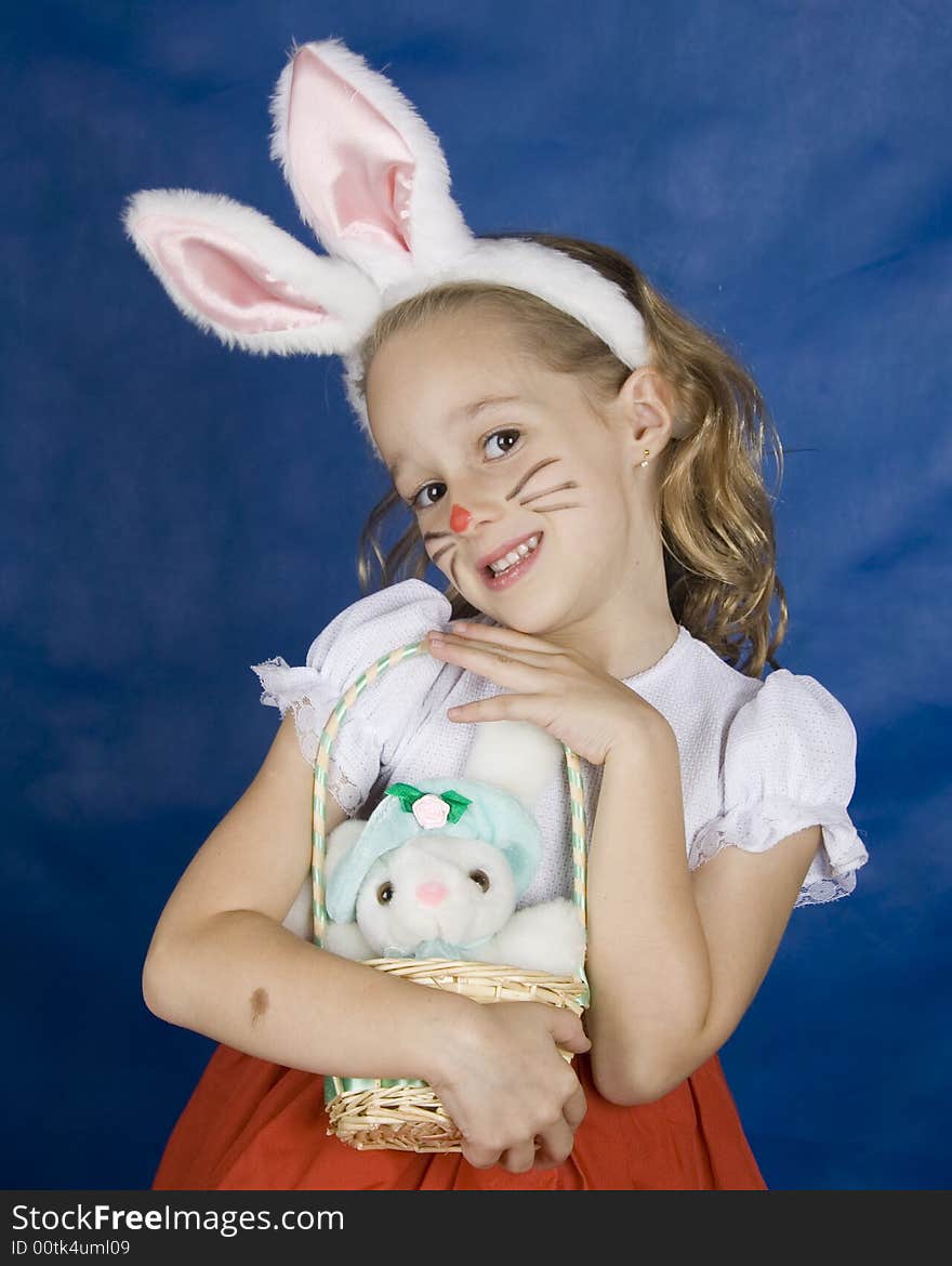 Little girl smilling with bunny in basket over blue background. Little girl smilling with bunny in basket over blue background