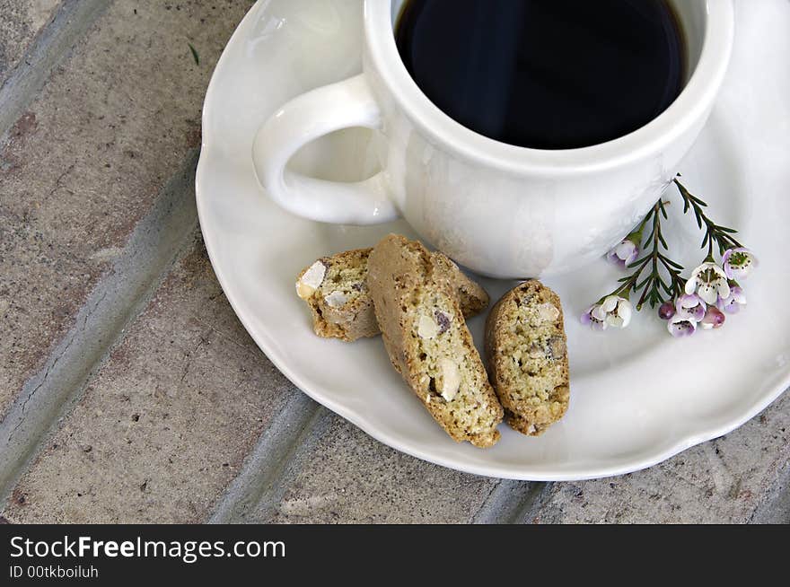 Cup of coffee with biscotti and small flowers on a brick background. Cup of coffee with biscotti and small flowers on a brick background.