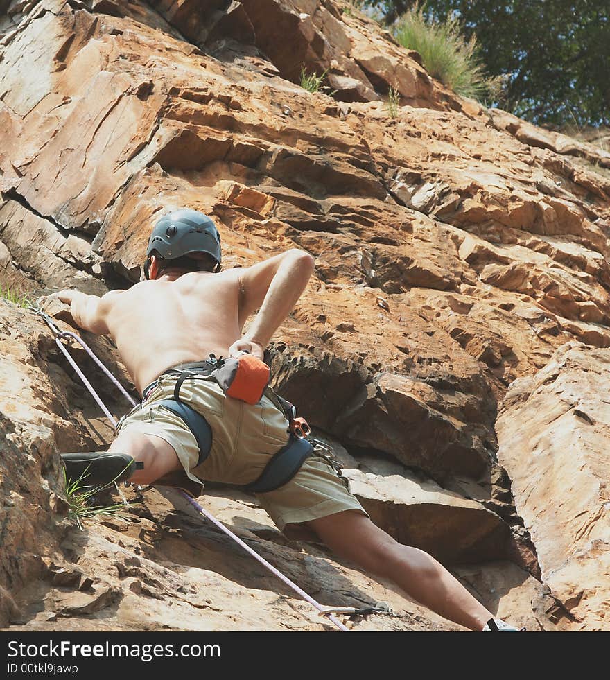 Man is mountain climbing in short pants with gear and helmot, equipment like ropes carabiners locks. Man is mountain climbing in short pants with gear and helmot, equipment like ropes carabiners locks