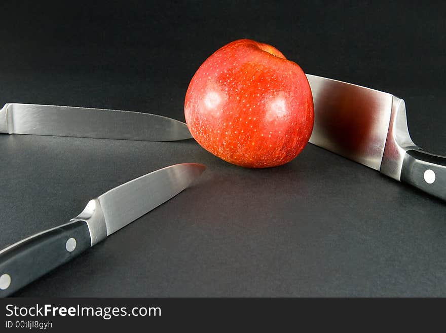 Bright red apple on dark background and three kitchen knives. Bright red apple on dark background and three kitchen knives