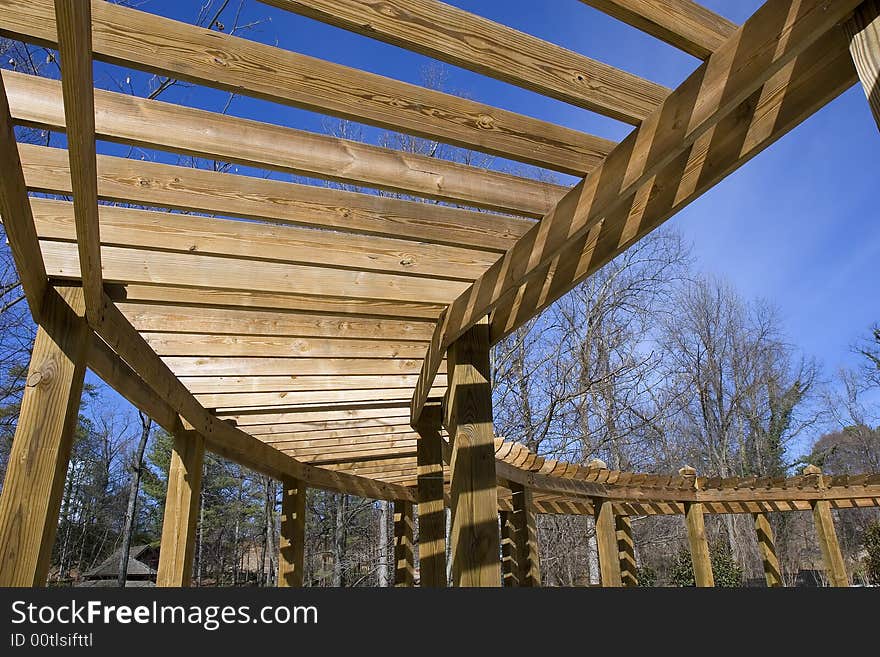 A curving wood structure hanging over a walkway in the park. A curving wood structure hanging over a walkway in the park