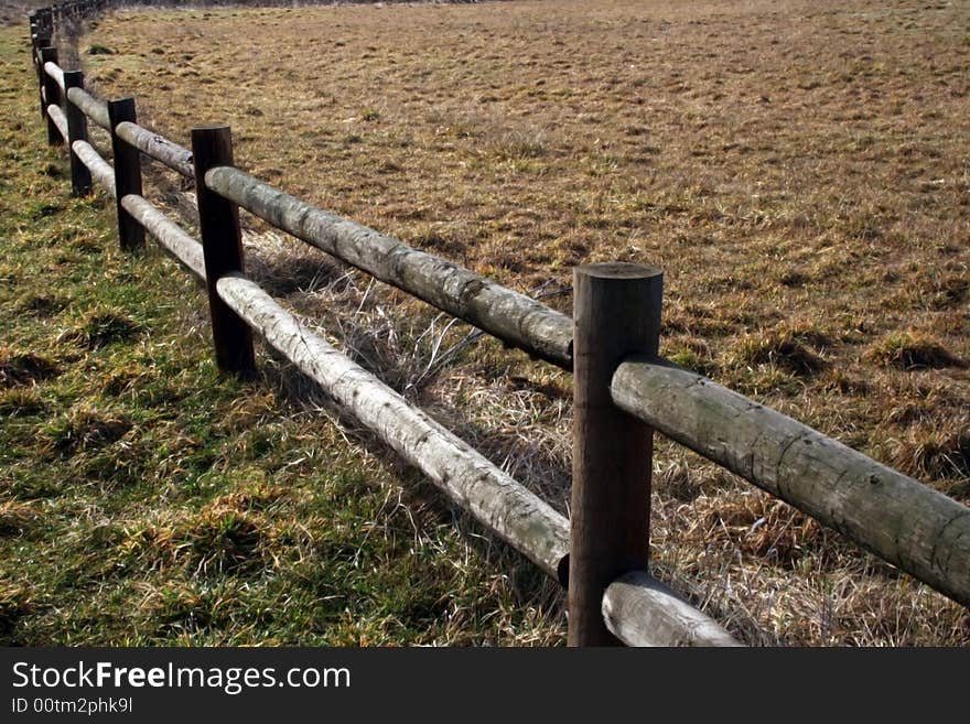 A wooden rail fence bordering a grass field. A wooden rail fence bordering a grass field.