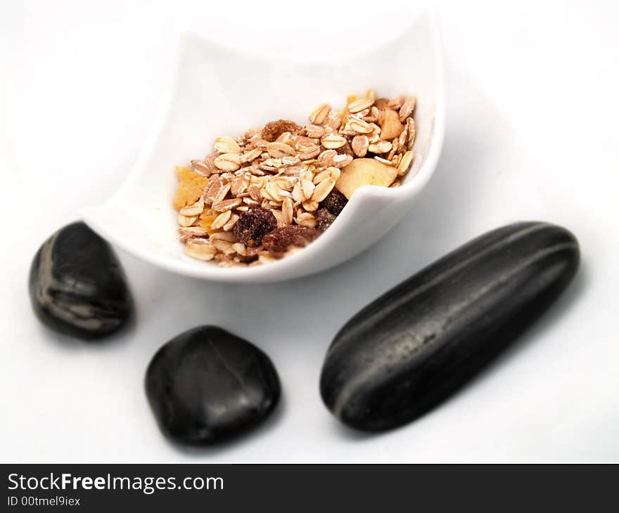 Several cereals in a white bowl, and some dark ying-yang stones