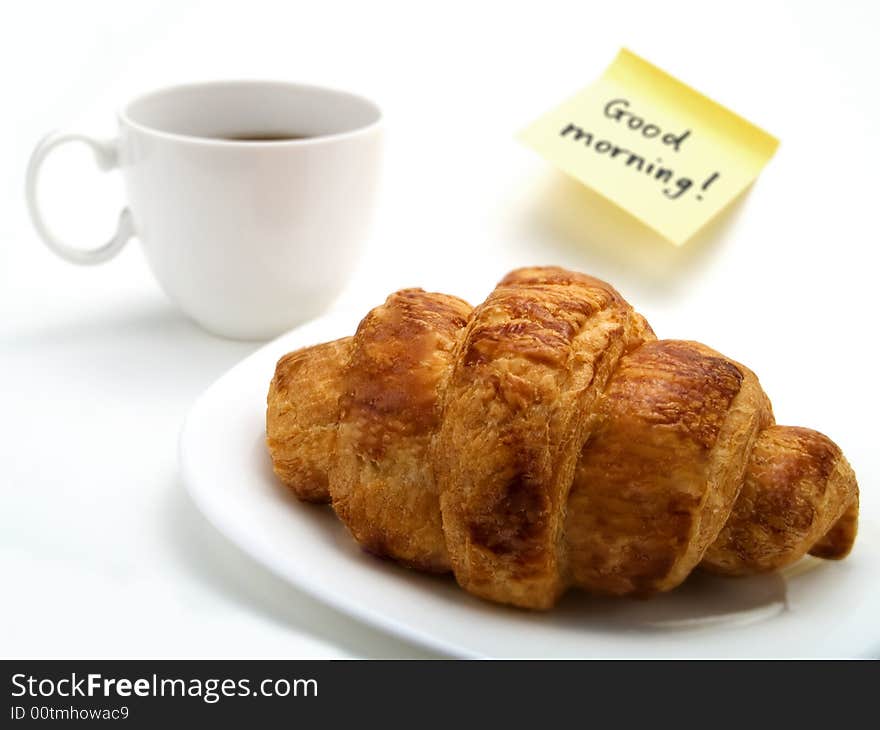 A croissant, a cup of coffee and a yellow note