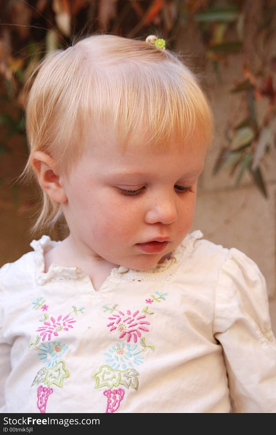 Toddler looking down with leaves behind her. Toddler looking down with leaves behind her