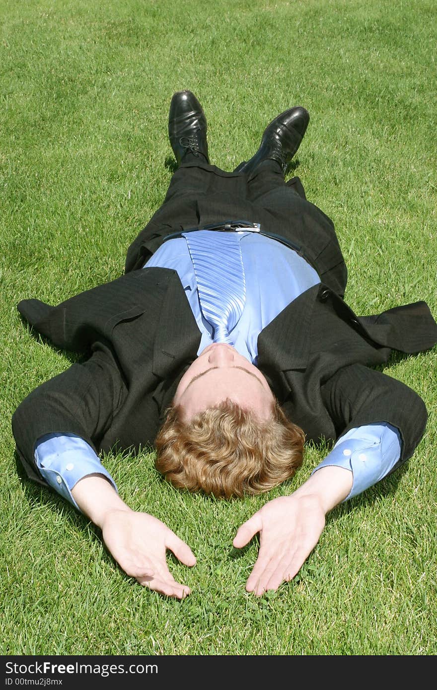 Single white businessman in suit stretches and relaxes on green grass. Single white businessman in suit stretches and relaxes on green grass